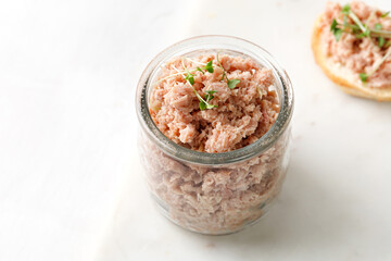 French tuna fish rillettes or pate with micro greens in glass jar and white background.