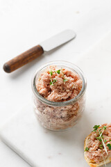 Healthy tuna pate or rillettes in a glass jar on marble board and white background.