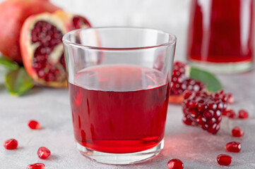 A glass of pomegranate juice with fresh pomegranate fruits on a gray concrete background. Vitamins and minerals. Healthy drink concept. Copy space.