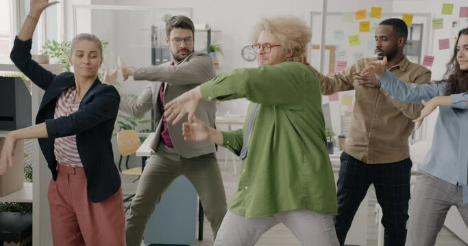 Crazy young employees are dancing in office moving arms smiling having fun at work. Corporate party and creative businesspeople concept.
