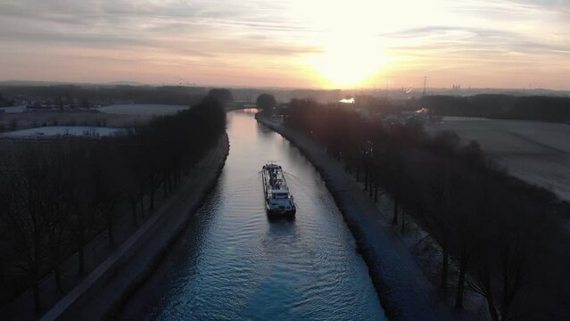 Drone shot dolly forward following a barge on the Scheldt river in the morning with fog and a beautiful golden sunrise on Tournai in Belgium