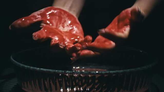 Female hands covered in blood washes her hands close-up in the dark. Bloody mess. Terrible bleeding. Crimson drops of blood fall to the surface. Scarecrows with blood.