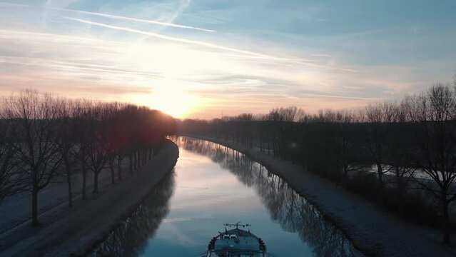 Drone shot dolly backward revealing a barge on the Scheldt river in the morning with fog and a beautiful golden sunrise on Tournai in Belgium