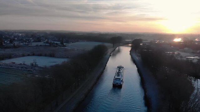 Drone shot dolly sideways above a barge on the Scheldt river in the morning with fog and a beautiful golden sunrise on Tournai in Belgium, next to wastewater treatment plant