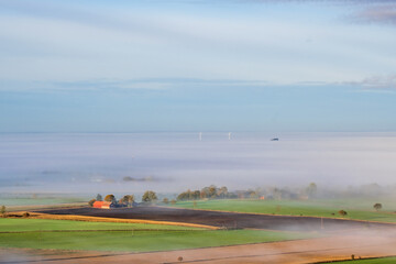 Fototapeta premium View at farm in the countryside with fog on the fields