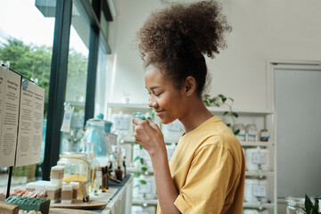 Young African American woman smells organic soaps, chooses and shops for reusable appliance products in refill store, zero-waste grocery, and plastic-free, environment-friendly, sustainable lifestyle. - obrazy, fototapety, plakaty
