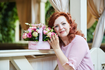 Portrait of a beautiful red-haired mature woman in a pink dress on the street.