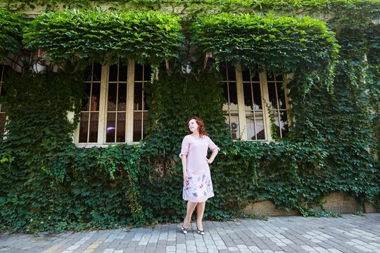 Beautiful Red-haired Mature Woman In A Pink Dress On The Street. In Full Growth.