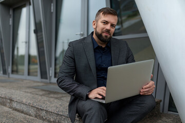 business man with laptop sitting on the steps of an office building, Concept of a successful real estate agent