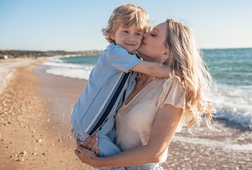 Mom and son are walking on the beacj, the woman hugs and kisses the child in her arms. people together.