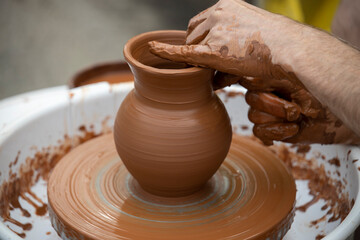 Fototapeta na wymiar Potter's hands working clay on a potter's wheel. Master making clay pottery.