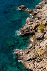 Fototapeta na wymiar Rocky limestone cliffs and rocky shore of Capri island in Italy surrounded by deep blue and turquoise mediterranean sea in Gulf of Naples. View point near “Marina piccola“ harbour and Capri village.