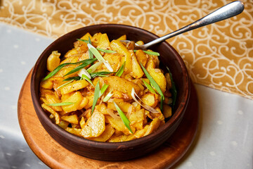 Cast iron plate with baked potato slices sprinkled with green onions on the table