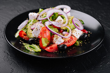 Greek salad in black bowl on stone
