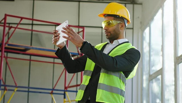 Charismatic businessman in a suit at construction site wearing safety equipment taking pictures of construction and analysing them