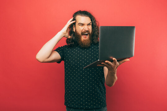 Photo of shocked young bearded man looking at laptop screen.