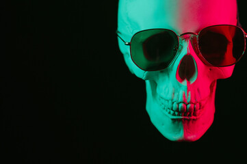 human skull wearing sunglasses with pink green neon light on a black background