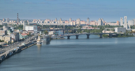 View of the buildings of the city. Wide river with bridges. The traffic of cars driving on the roads. Wide shot, daytime, blue sky. Europe, Ukraine, Kyiv.