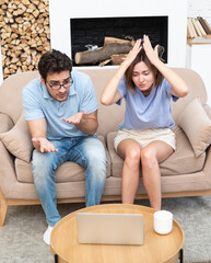 Young excited couple sitting on couch and watching movie or game on laptop. Leisure time and resting concept