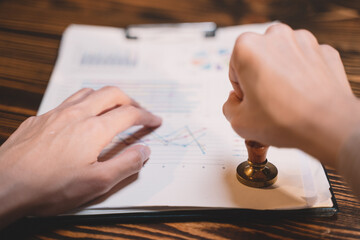 A seal to show approval of an agreement or contract by an authorized person. A businesswoman is about to stamp a document at the office legally. The boss signs the certificate or letter on the desk.