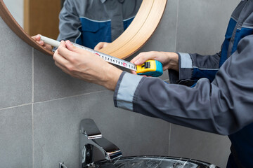 Close-up photo of handyman metering mirror in bathroom with measuring tape