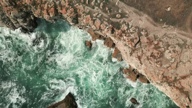aerial top down rocky coastline cliff with ocean waves crashing on to beach 
