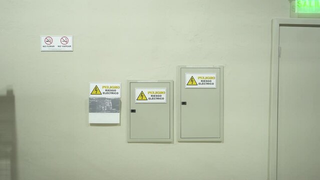 Wall with electrical panel and warning signs in a warehouse near the exit door
