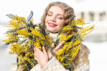 Portrait of a young woman with blond hair holding a bouquet of mimosa in her hands. Spring