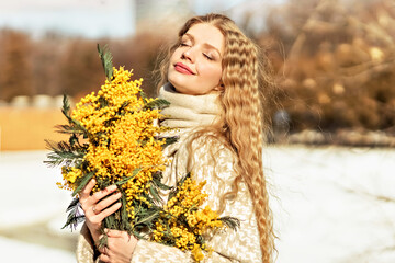 Portrait of a young woman with blond hair holding a bouquet of mimosa in her hands. Spring