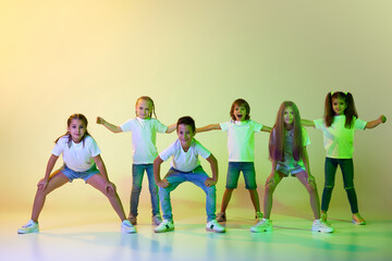 Group of children, active kids in sportive casual style clothes dancing in choreography class isolated on green background in yellow neon light.