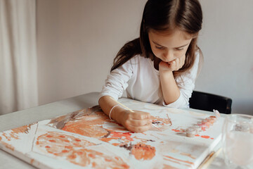 Happy preschooler girl paints a picture by numbers with a brush and gouache. Home entertainment and...
