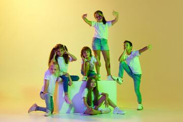 Obraz premium Dance class. Joyful children, kids in t-shirts and jeans dancing in action isolated on green background in yellow neon light.