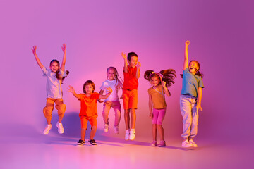 Dance group of happy, active little girls and boys in bright clothes in action isolated on pink background in neon. Concept of music, fashion, art, childhood
