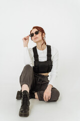beautiful red-haired woman in full growth in rough trousers and a vest and rough black boots on a white background. fashionable women's clothing 2023. clothing and fashion concept