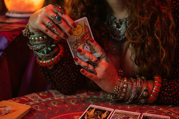close-up of the hand of a pythoness with a lot of jewellery and accessories holding a tarot card.