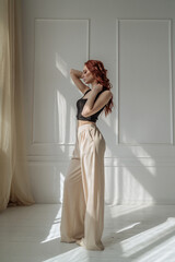 beautiful young red-haired woman in a tank top and wide trousers in the studio. model in trendy elegant clothes. female fashion and beauty concept