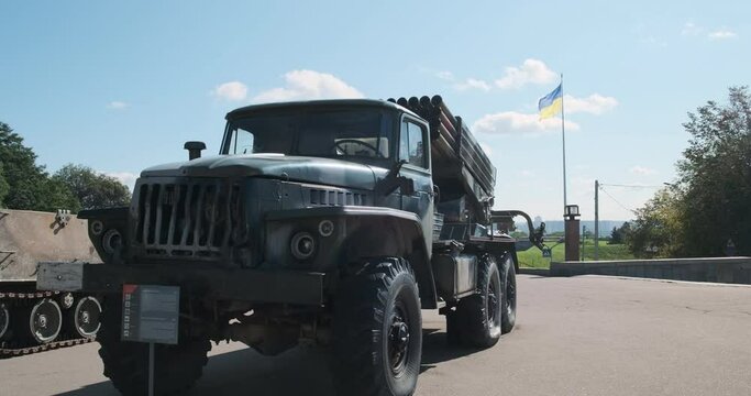Grad multiple launch rocket system, standing in the open-air museum in Kyiv, Ukraine. The flag sways in the wind against the background, blue sky, daytime.