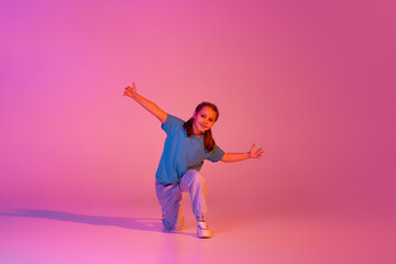 Fototapeta Portrait of caucasian little girl, kid in casual bright clothes dancing isolated over pink background in neon. Action, dance, happy childhood obraz