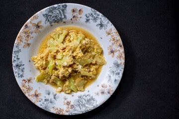 a plate of fried vegetables on black background, top view