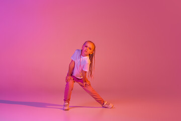 Fototapeta Moves. Cute little girl, kid in casual bright clothes dancing isolated over pink background in neon. Action, dance, happy childhood obraz