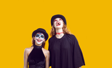 Emotional family of mother and teenage daughter celebrating Halloween and laughing madly together. Crazy girls with creative Halloween face art isolated on orange background. Halloween concept.