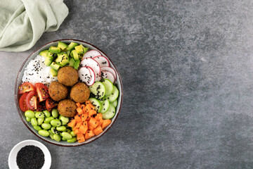 Buddha bowl with rice, falafel, green beans, cherry tomatoes, avocado, cucumbers, black sesame on a...