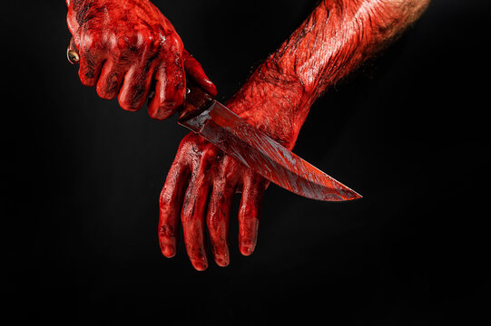 A man wipes a bloody knife with his hand on a black background. 