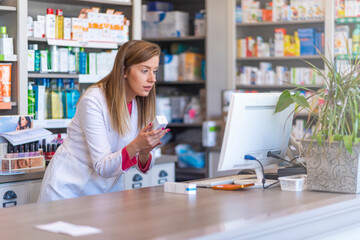 Pharmacist making prescription record through computer in pharmacy. Portrait of female pharmacist working with computer behind counter in pharmacy - obrazy, fototapety, plakaty