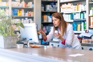 Portrait of pharmacist standing at counter in pharmacy. Pharmacist using the computer at the...