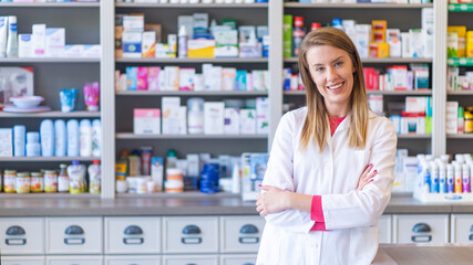 Portrait of a smiling pharmacist with arms crossed at modern pharmacy. Beautiful woman wearing in...