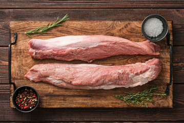 Raw meat pork tenderloin on  wooden cutting board ready to cook. Seasonings for pork tenderloin...