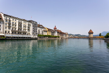 Fototapeta na wymiar LUCERNE, SWITZERLAND, JUNE 21, 2022 - View of the old buildings and the wodden covered Kapellbrucke Bridge on the background on the Reuss river in city center of Lucerne, Switzerland