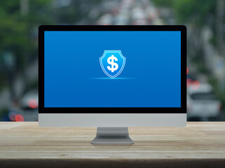 Dollar with shield flat icon on desktop modern computer monitor screen on wooden table over blur of...