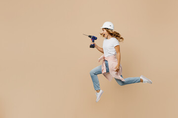 Full body young young employee laborer handyman woman in white t-shirt helmet hold drill jump high isolated on plain beige background Instruments accessories for renovation room Repair home concept.